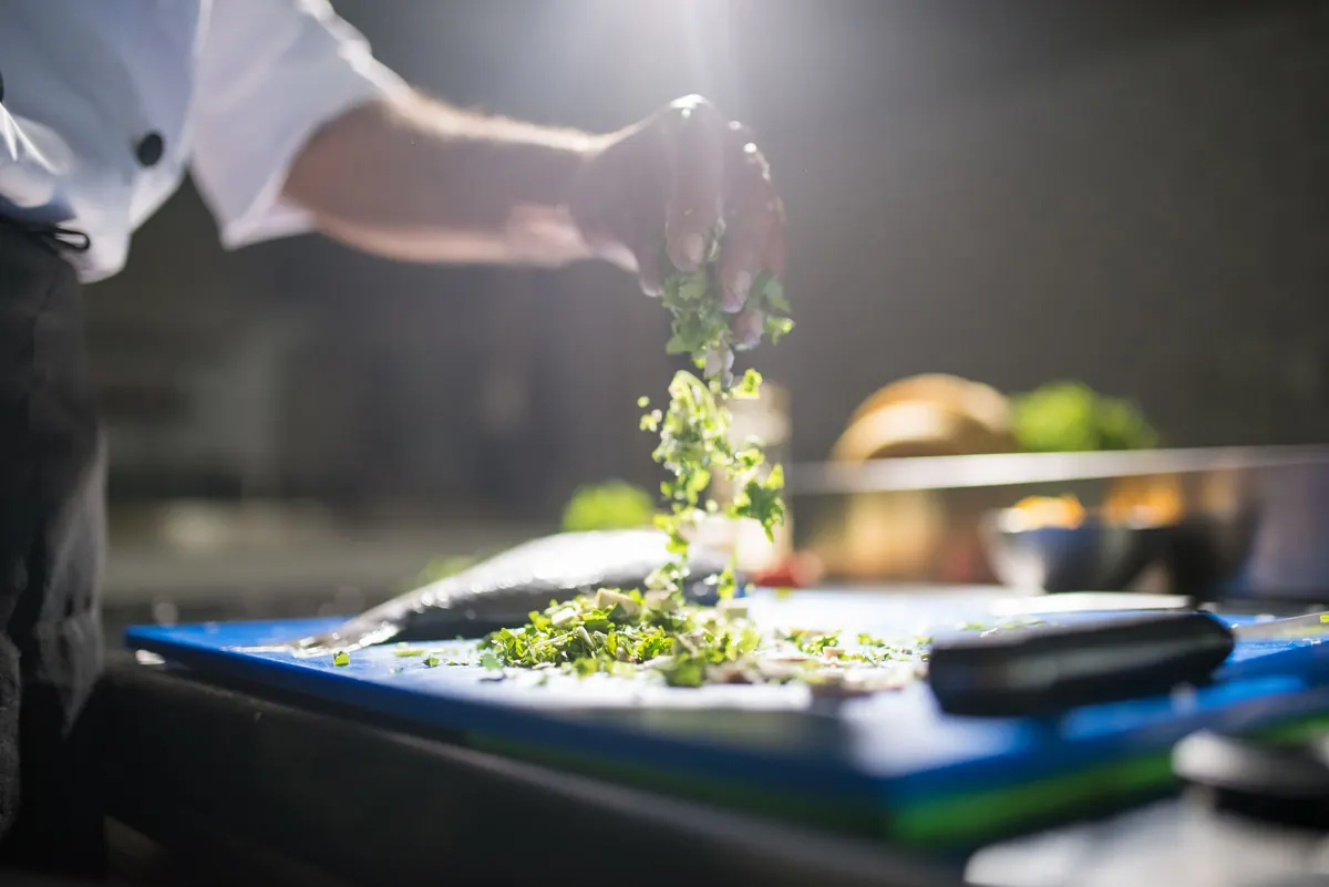En cuisine professionnelle, un cuisinier verse des restes de préparation depuis sa planche